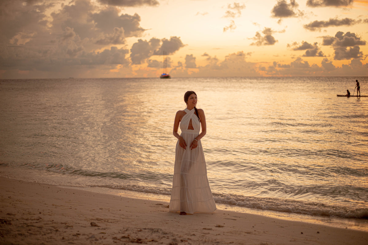Woman wearing a white Bohème by Ena outfit by the sea at sunset