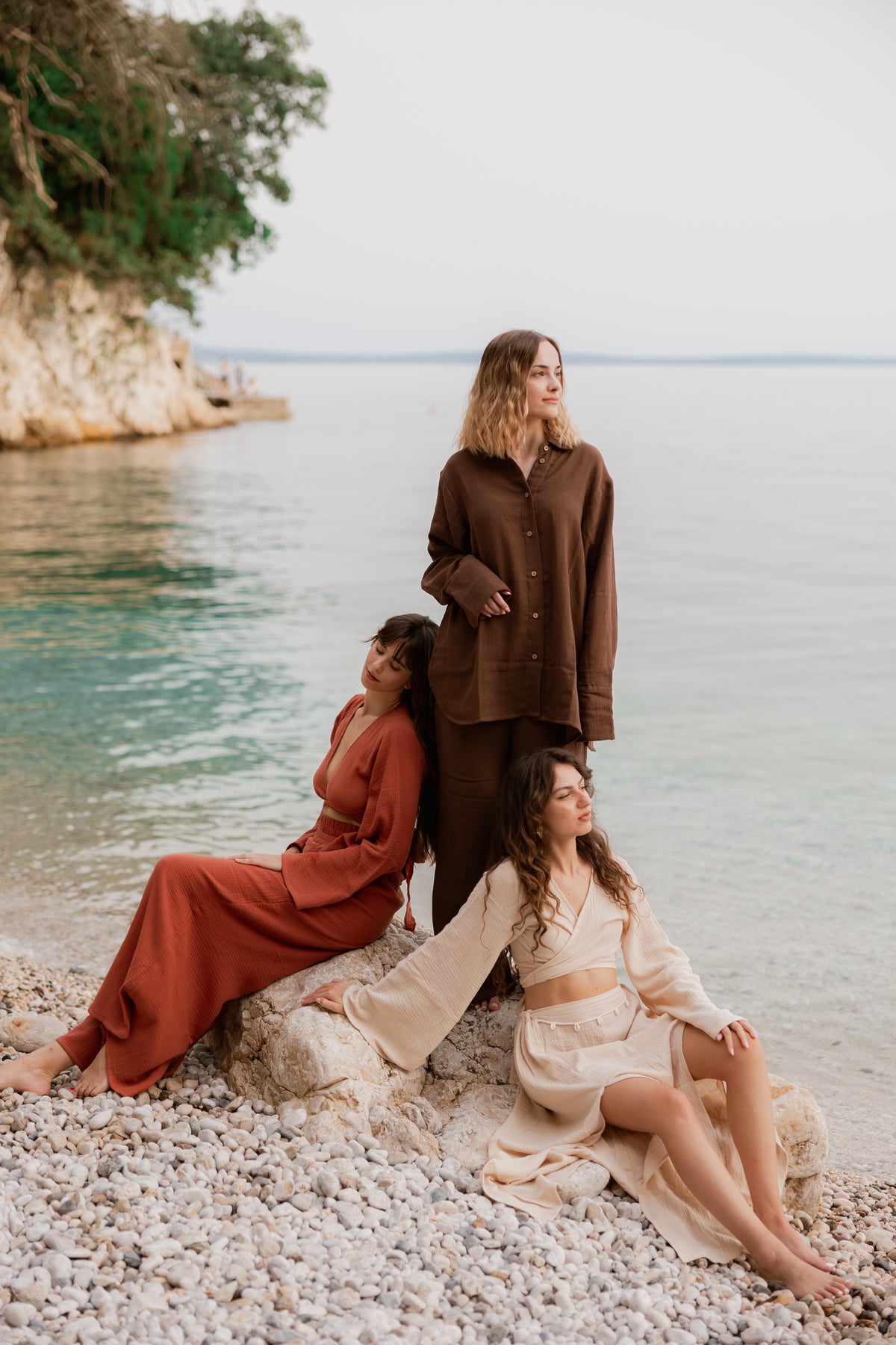 Three women wearing mix and match Bohème by Ena outfits in brown, terracotta and cream by the sea