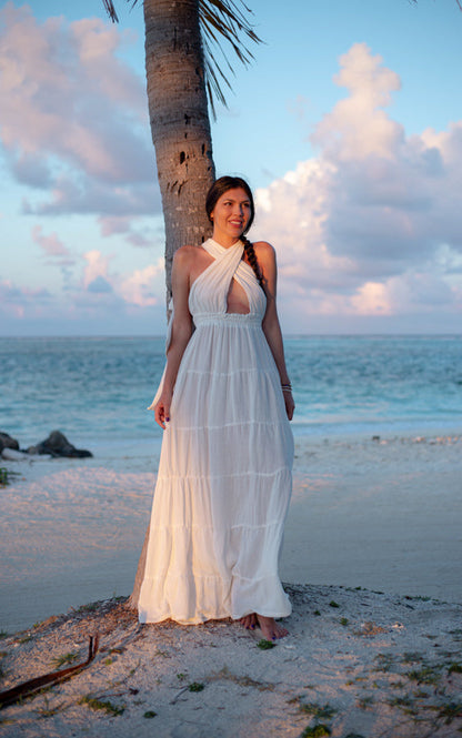 Woman wearing the white Esmeralda Maxi Dress beside a palm tree on the beach