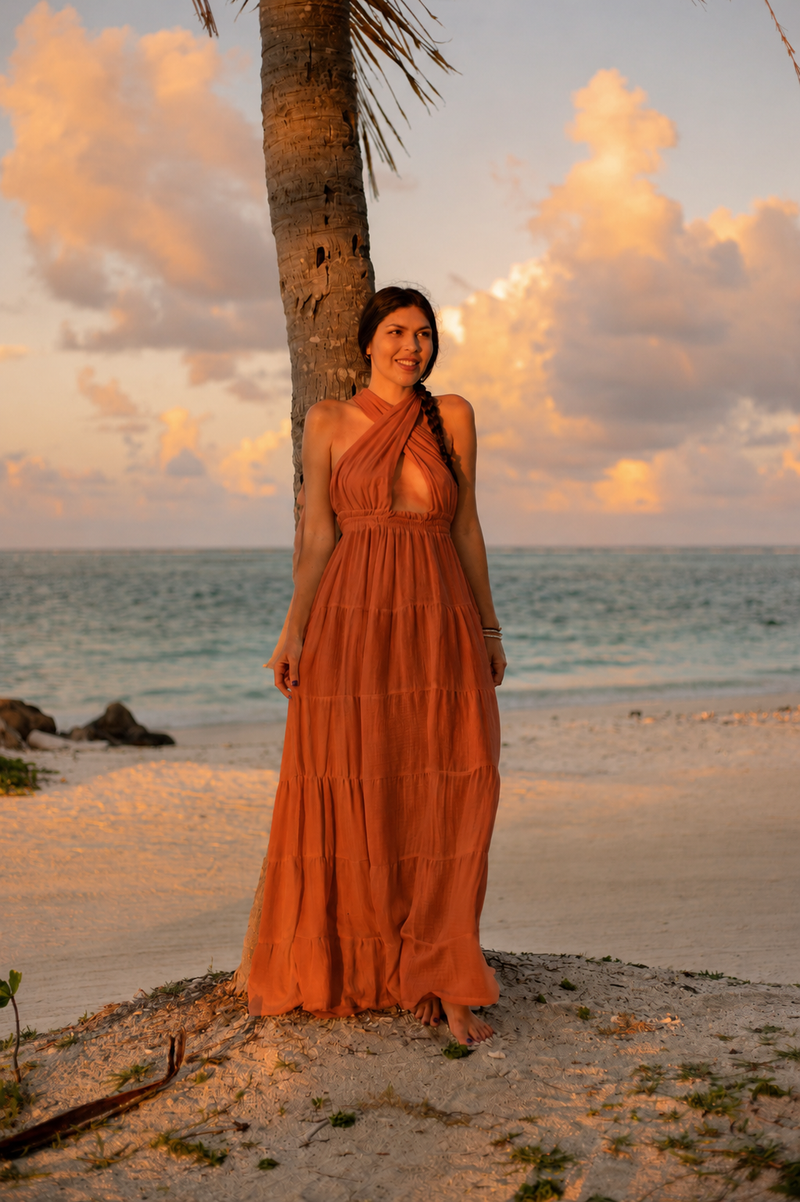 Woman wearing the terracotta Esmeralda Versatile Maxi Dress on the beach at sunset