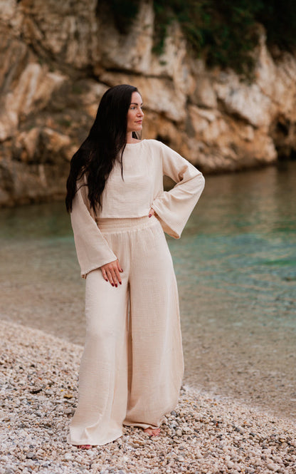 Woman wearing the sand Oasis organic cotton matching set with wide-leg pants by the sea