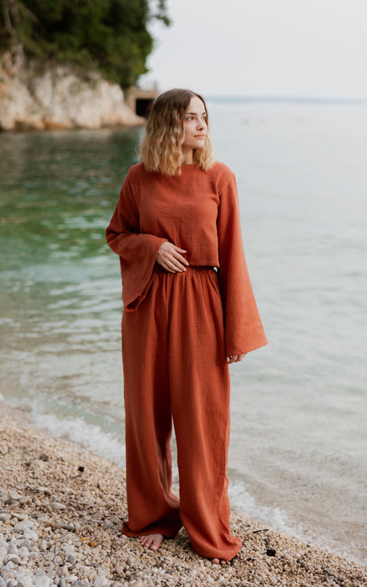 Woman wearing the terracotta Oasis matching set with flowing top and wide-leg pants by the sea